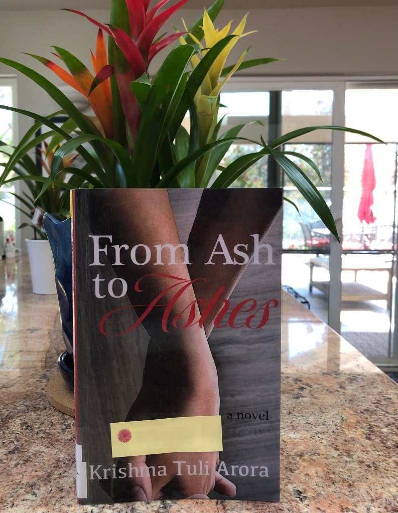 The cover of From Ash to Ashes on a granite counter with a plant in the background.